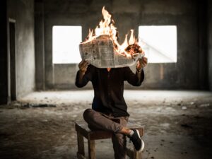 Muž v opuštěné budově držící hořící noviny.
